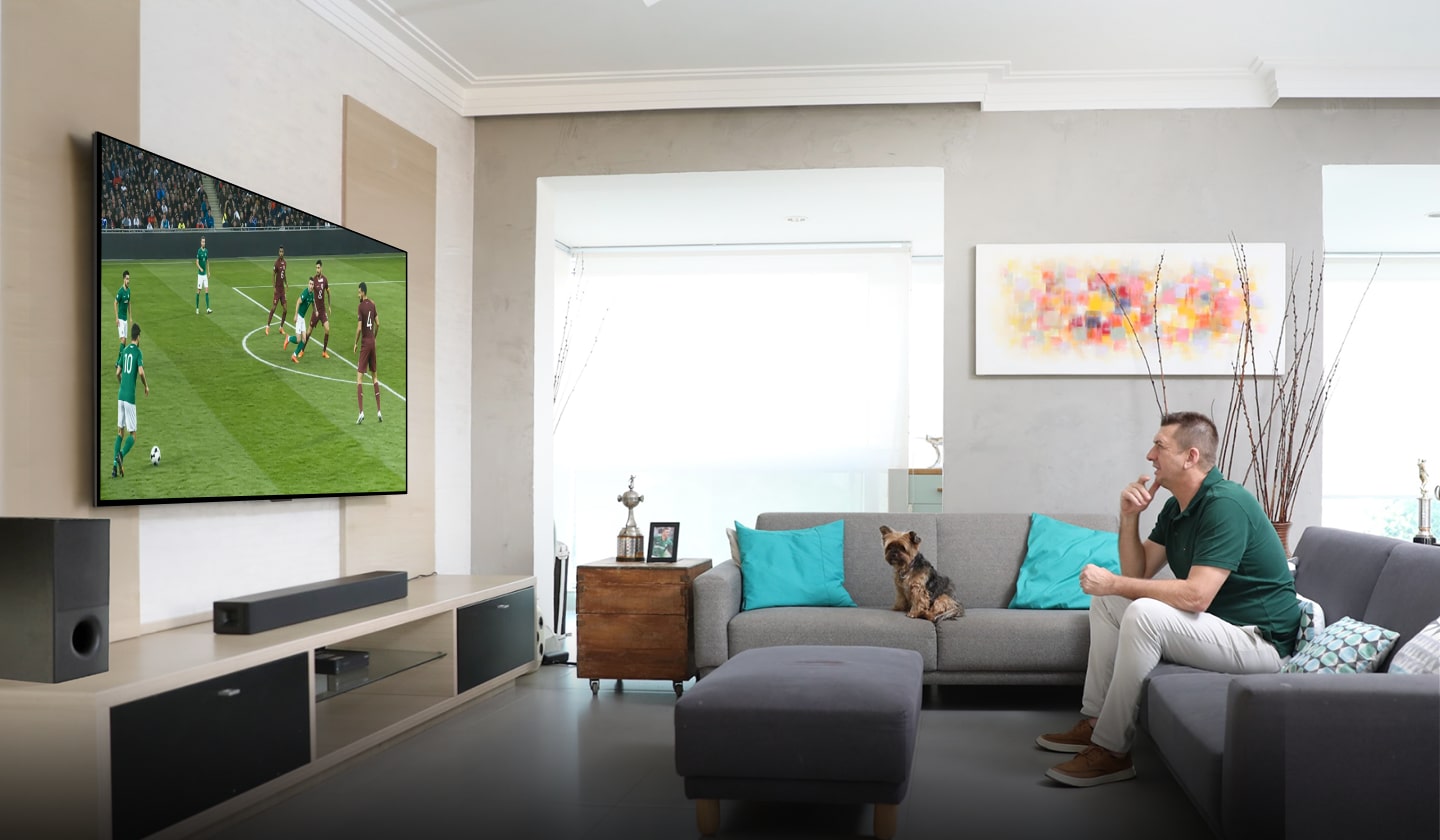 Marcos, sentado cómodamente en el sofá de su sala, observa con interés y analiza un partido de fútbol en su televisor LG de gran tamaño.