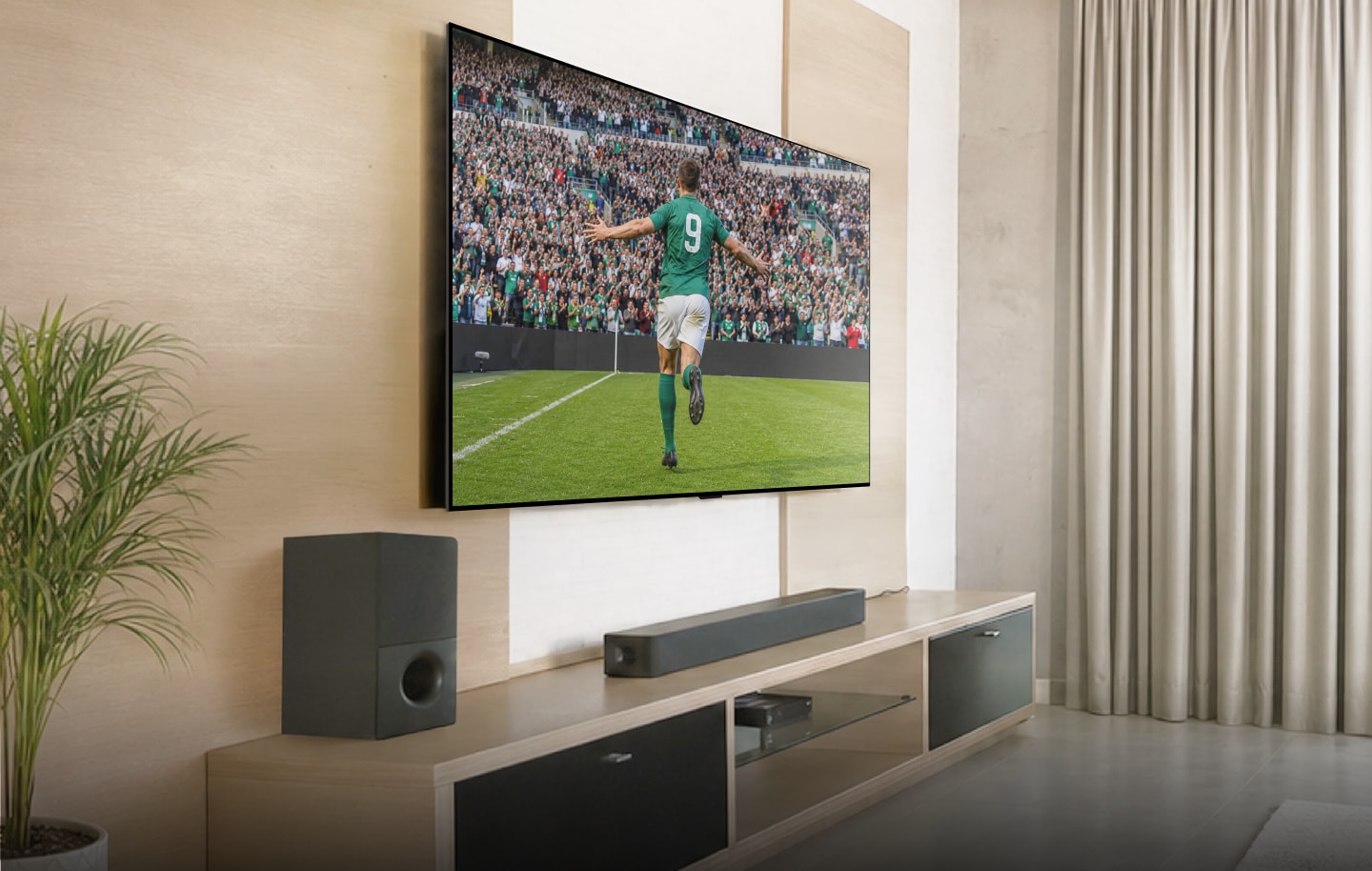 Gran televisor LG montado en la pared con una barra de sonido y un subwoofer, mostrando a un futbolista celebrando un gol.
