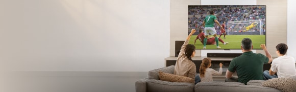 Una familia sentada en el sofá de la sala disfruta y celebra un partido de fútbol en una pantalla grande.