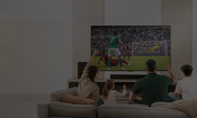 Una familia sentada en el sofá de la sala disfruta y celebra un partido de fútbol en una pantalla grande.