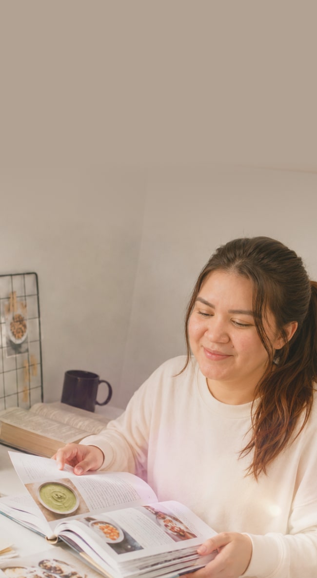 Una mamá planea las comidas de su bebé mientras consulta un libro de recetas en su escritorio.