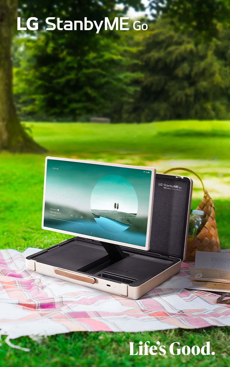 LG StanbyME Go se coloca sobre una manta de picnic a cuadros con el lado izquierdo hacia adelante y muestra una pantalla de inicio con el tema del clima.