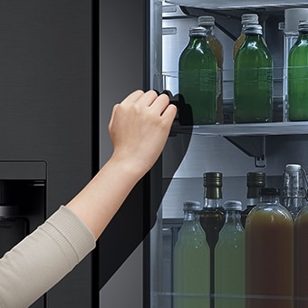 Vista frontal de refrigerador InstaView de cristal negro con la luz interior encendida. Manos tocando la pantalla InstaView.