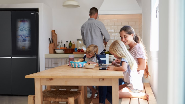 Una familia en una cocina moderna con refrigerador LG side by side a la derecha.