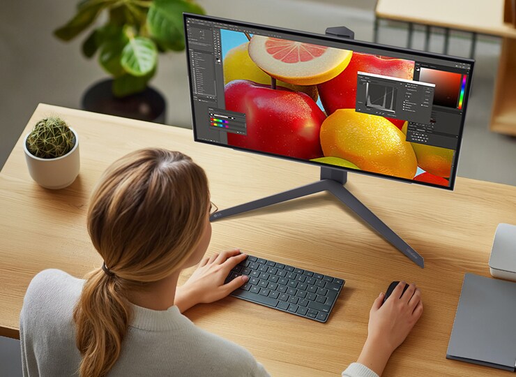 Persona editando una imagen vibrante de frutas en un monitor LG con audífonos.