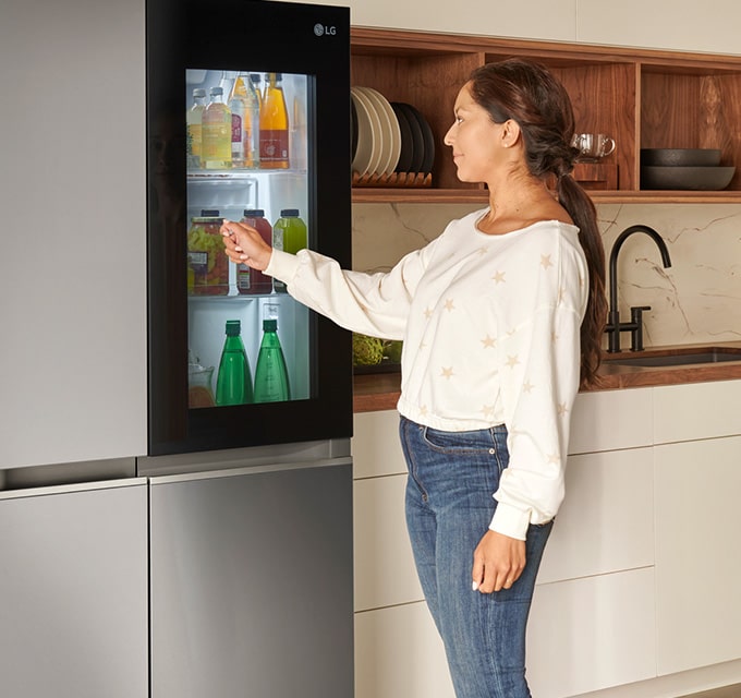 Mujer usando la función InstaView Door-in-Door de LG, mostrando el interior iluminado del refrigerador.