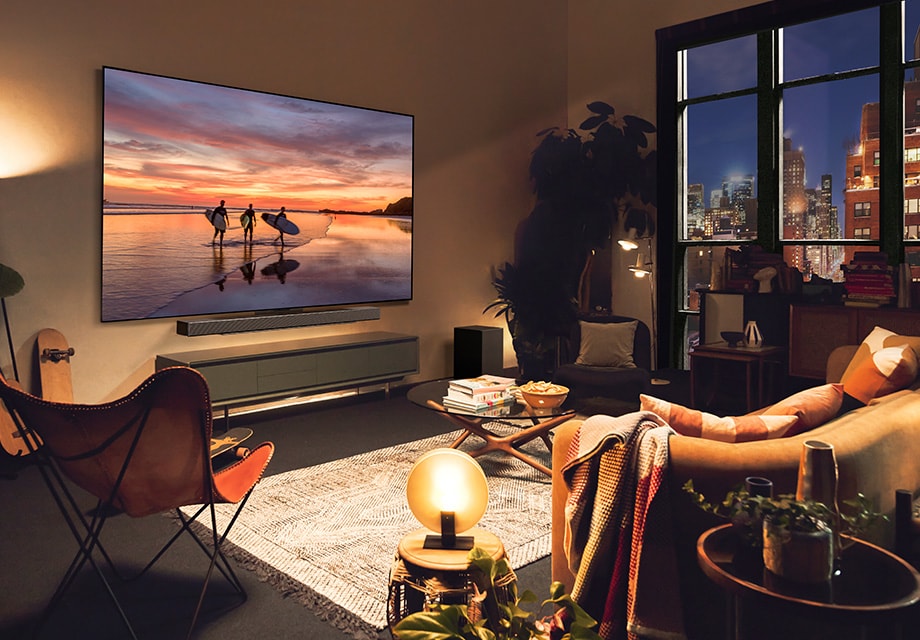 Sala de estar con iluminación ambiental y LG OLED TV mostrando una escena de playa al atardecer, con luces cálidas, plantas y decoración moderna