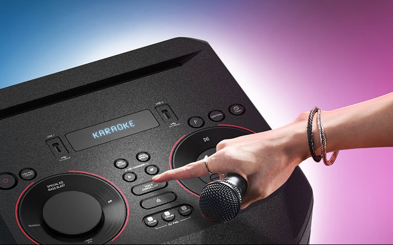 Una mano sosteniendo un microfono, tratando de presional el botón de Cancelador de Voz en la parte superior de LG XBOOM.