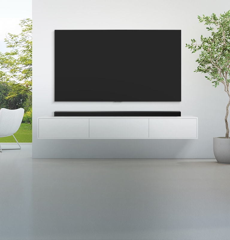 Un televisor y una barra de sonido están colocados en una amplia sala de estar blanca, y hay una vista del bosque verde afuera que se ve desde la amplia ventana.
