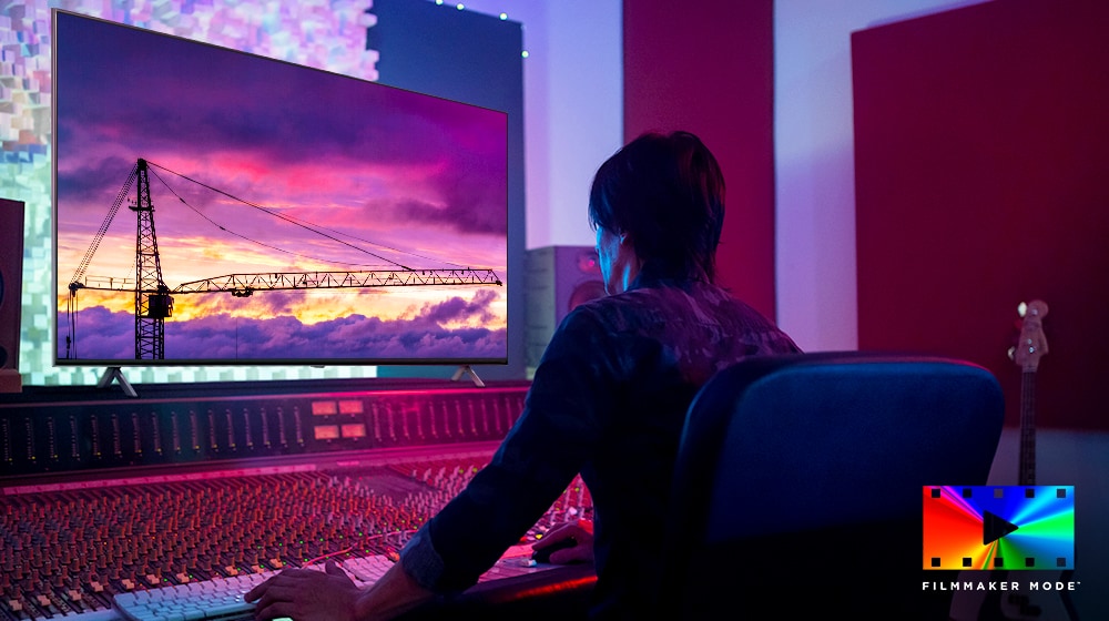 Un director de cine está mirando un gran monitor de televisión, editando algo. La pantalla de televisión muestra una grúa torre en un cielo violeta. El logotipo del modo FILMAKER se encuentra en la esquina inferior derecha. 