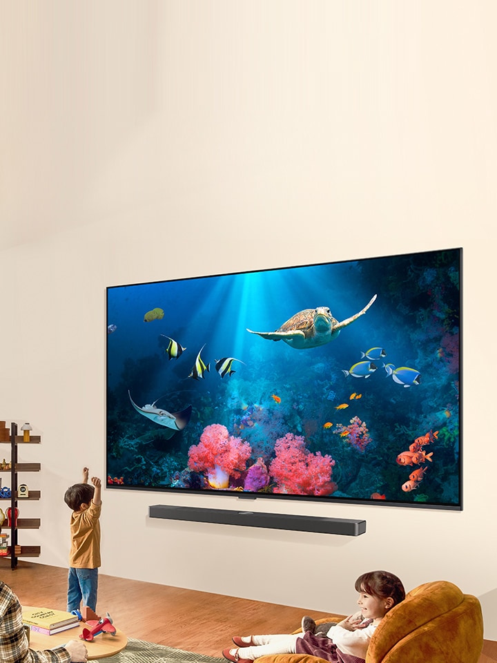 Una familia mira una brillante escena acuática en un TV LG QNED con una barra de sonido LG, en una sala de estar luminosa y natural.