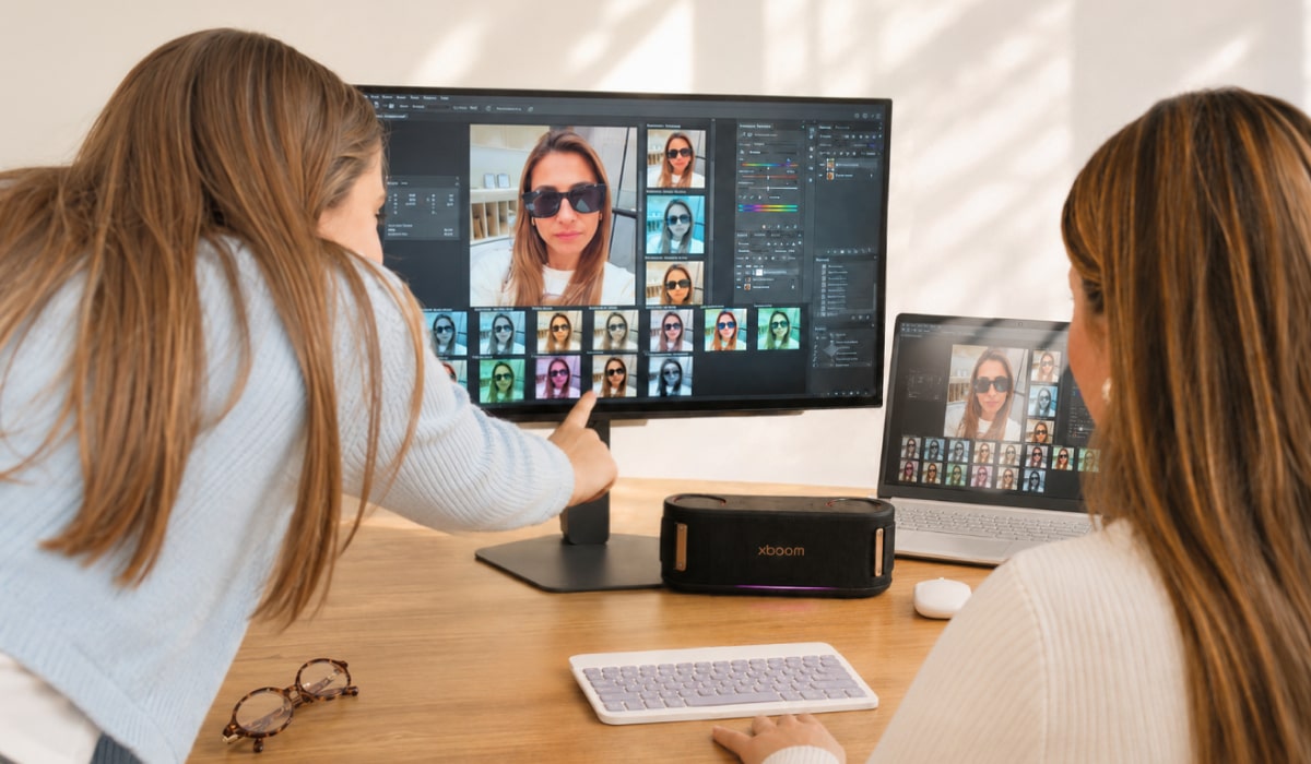 Dos personas revisando fotos de retrato en el monitor LG, con el parlante xboom y un portátil en el escritorio