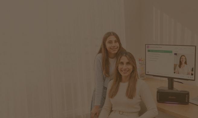 Una madre y su hija sonríen mientras están frente a un monitor de computadora LG que muestra una plataforma de aprendizaje en línea. El monitor muestra la pantalla "Ciencia y conocimiento científico", junto con una opción de videollamada que muestra a una maestra en línea. Un altavoz LG XBOOM está ubicado en el escritorio frente al monitor.