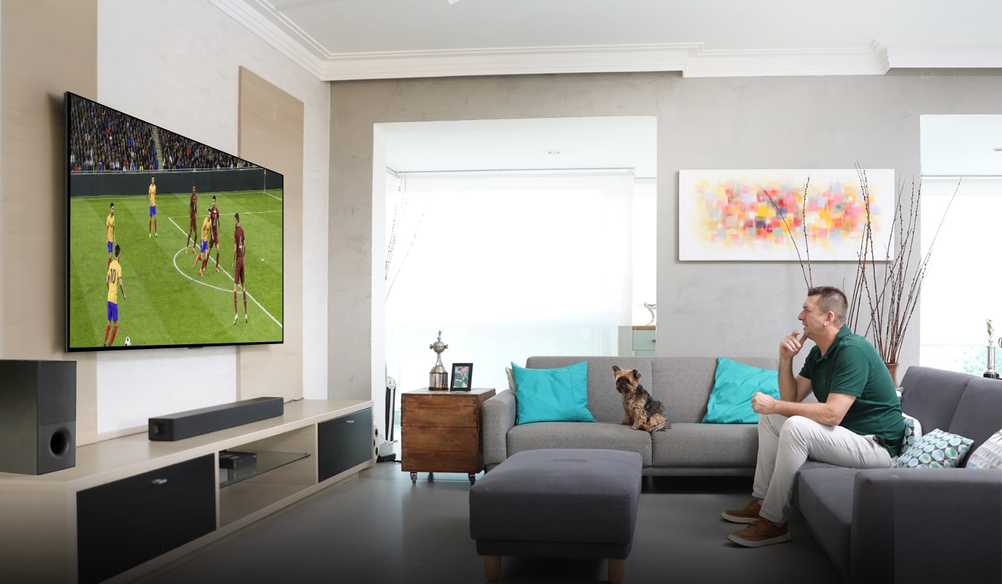 Marcos, sentado cómodamente en el sofá de su sala, observa con interés y analiza un partido de fútbol en su televisor LG de gran tamaño.