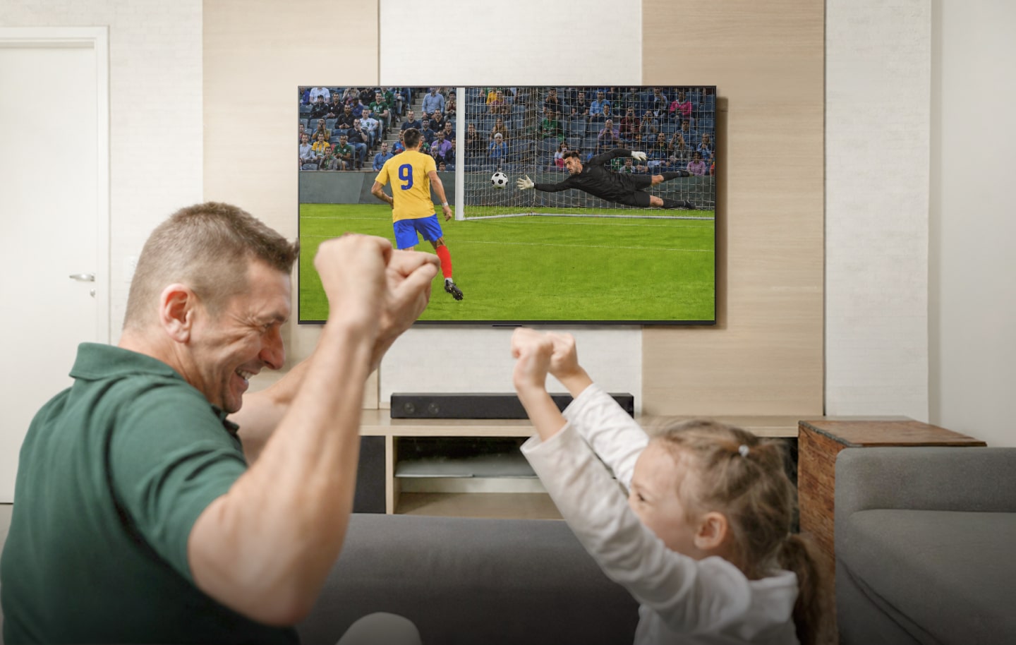 Família comemorando enquanto assiste a um jogo de futebol, com soundbar e subwoofer em destaque