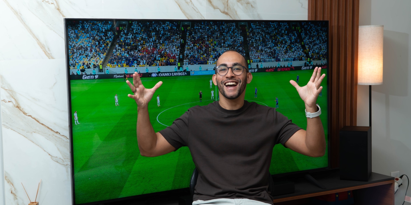 Rapael celebrando con las manos levantadas mientras ve un partido de fútbol en una pantalla vívida y nítida