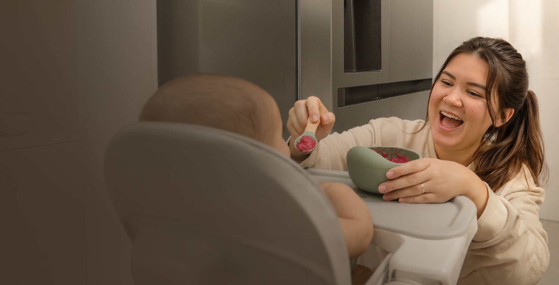 Una mamá alimenta a su bebé con papilla mientras está sentado en su silla alta, en la cocina.