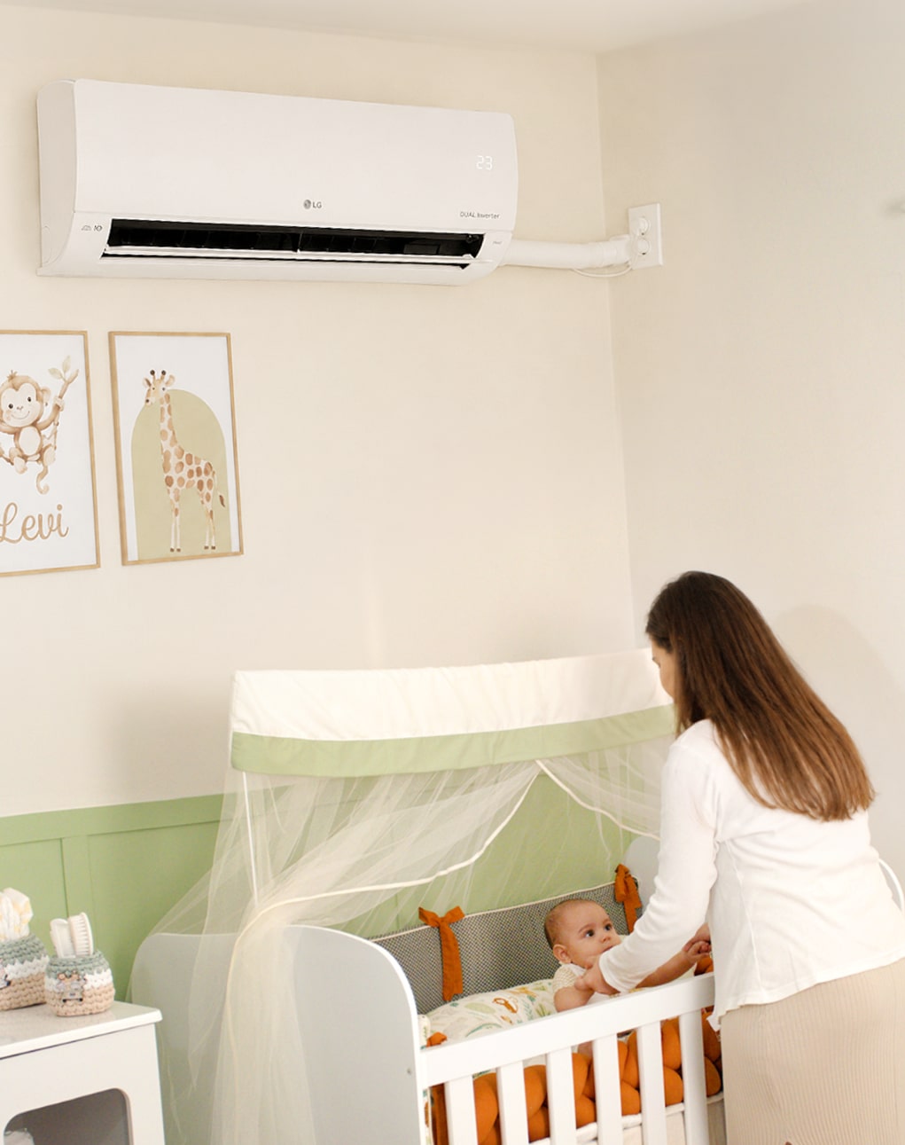 Una mamá toca las manos de su bebé en la cuna, bajo un aire acondicionado LG de pared.