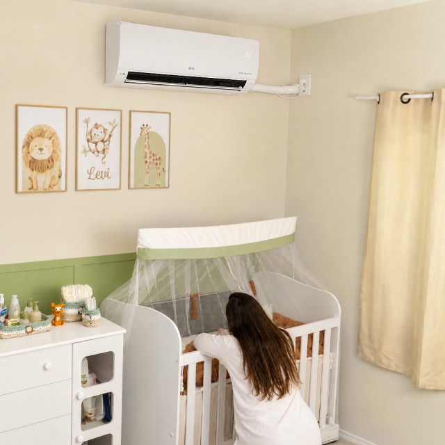 Una mamá se inclina sobre la cuna en la habitación del bebé, bajo un aire acondicionado LG de pared.