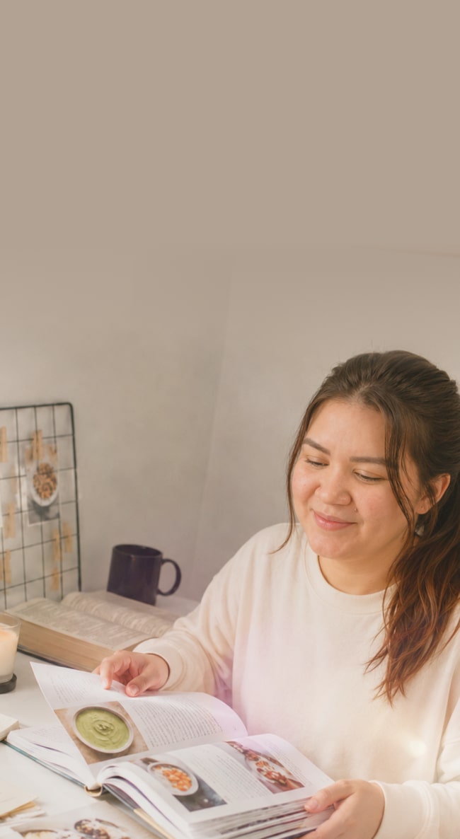 Una mamá planea las comidas de su bebé mientras consulta un libro de recetas en su escritorio.