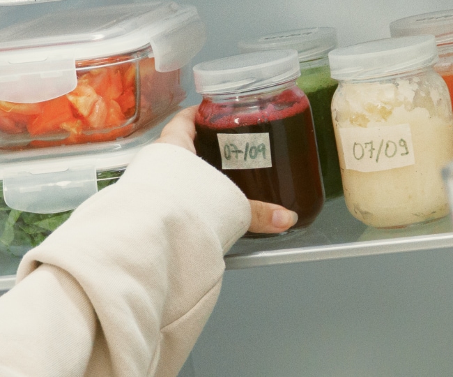Una mamá que carga a su bebé saca una bebida de una nevera LG Side by Side organizada con alimentos y bebidas.