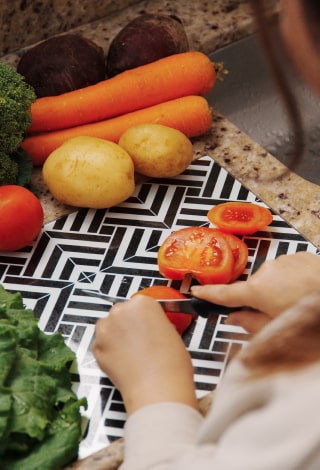 Una mamá corta un tomate junto a zanahorias, papas, brócoli y verduras de hoja.