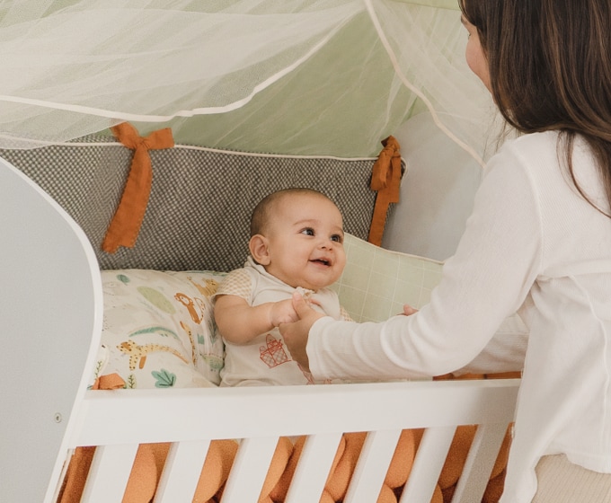 Una mamá sostiene las manos de su bebé acostado en la cuna.