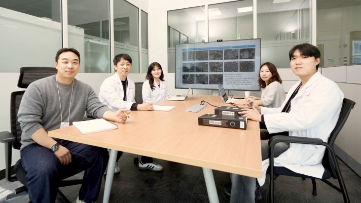 5 personas reunidas alrededor de una mesa con una pantalla que mostraba datos de microscopía.