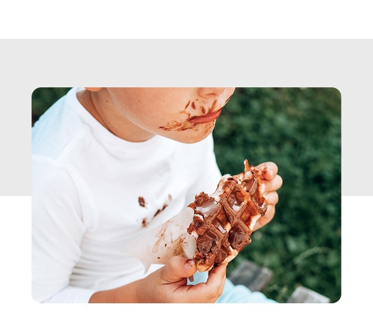 There is a child eating waffles and chocolate is on his face and clothes