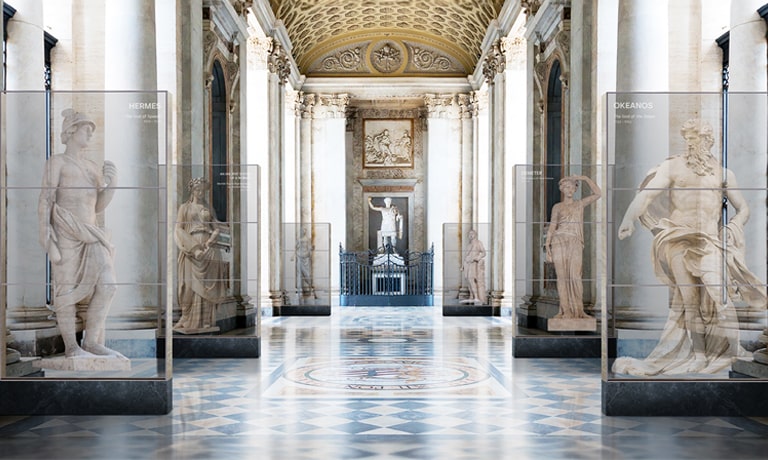 Pantallas OLED transparentes en pasillos del museo muestran estatuas antiguas e información, apiladas verticalmente.