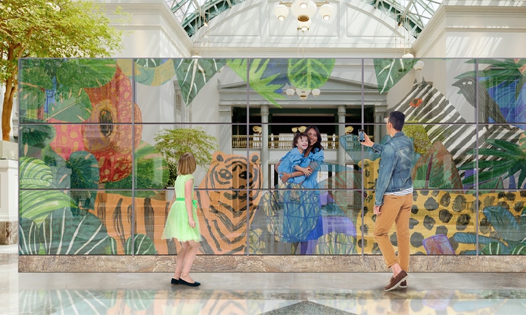 Una familia se toma una foto frente a una pared OLED transparente, con animales y plantas en la pantalla.