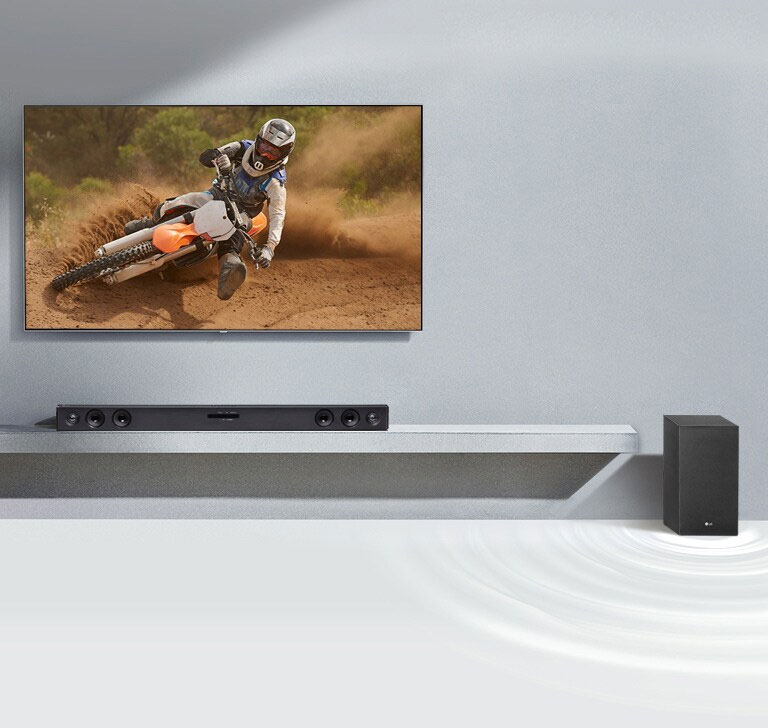 La barra de sonido LG SQC2 y el televisor LG están situados juntos en el salón. El subwoofer está situado junto a la barra de sonido. El televisor está encendido y muestra una imagen panorámica.