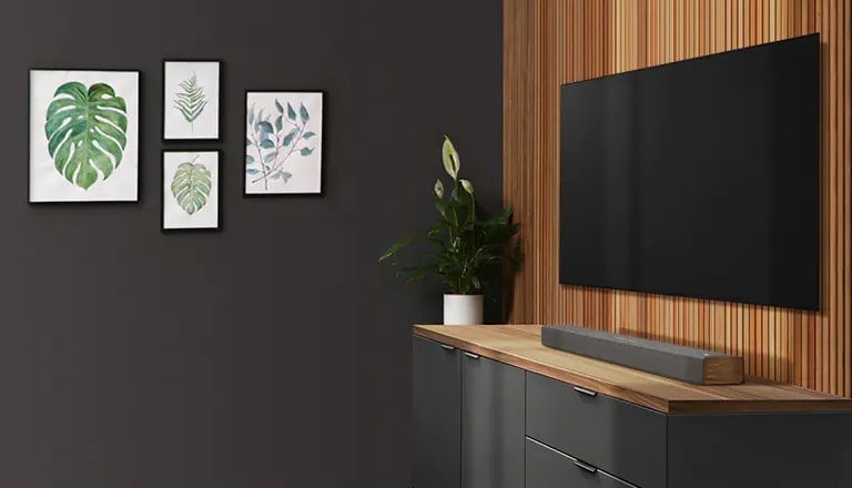Una barra de sonido y un televisor están colocados en una pared en tono de madera. Hay cuatro marcos de fotos colgados en la pared oscura.