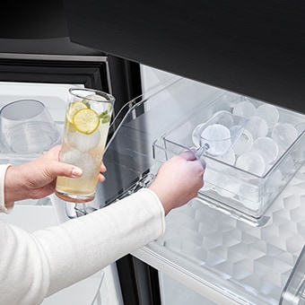 Una persona sostiene un vaso que contiene una bebida en una mano y recoge hielo artesanal en la otra.