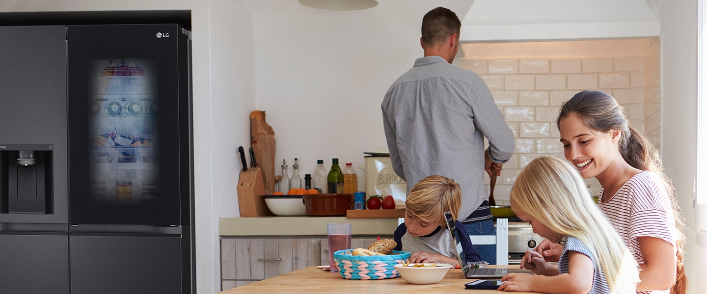 Toda la familia está sentada a la mesa preparando una comida. El refrigerador InstaView instalado en un lado de la cocina está creando aire frío rápidamente.