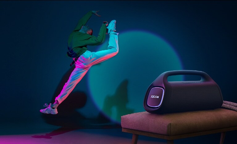 LG XBOOM GO XG9 está sobre la silla. Proyecta una luz de escenario en la pared y una persona baila frente a ella.