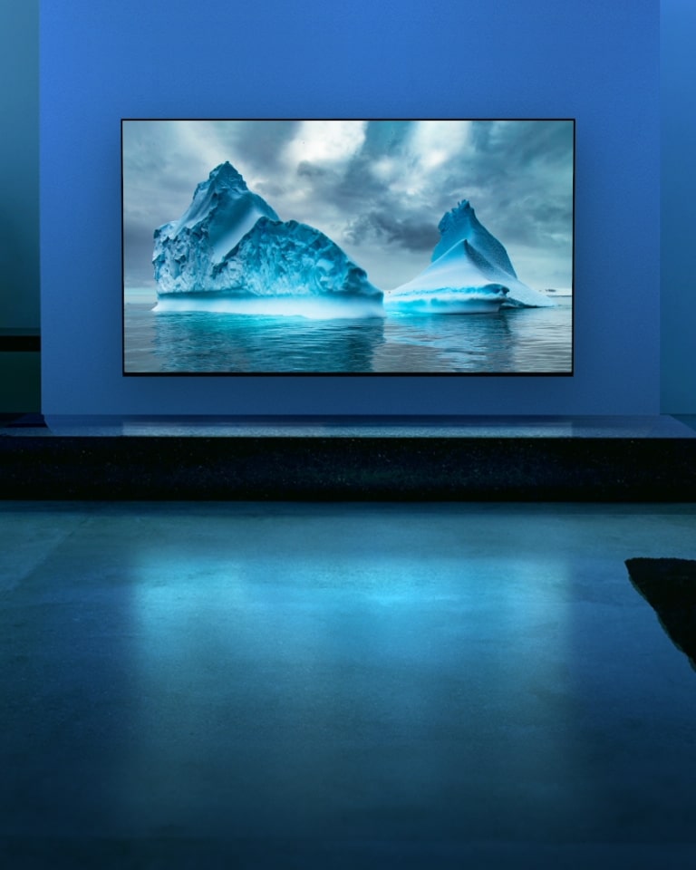 Un circuito de neón azul se mueve alrededor de la imagen del glaciar azul. La cámara se aleja y muestra este glaciar azul en la pantalla del televisor. El televisor está colocado en una amplia sala de estar con fondo azul.