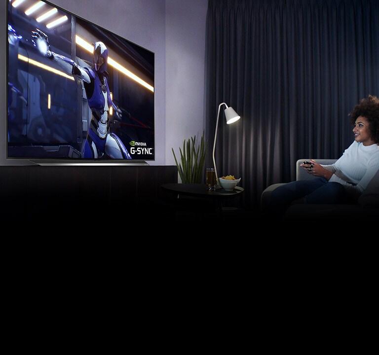 Mujer sentada en un sofá, sosteniendo un joystick mientras juega un juego en una pantalla de TV