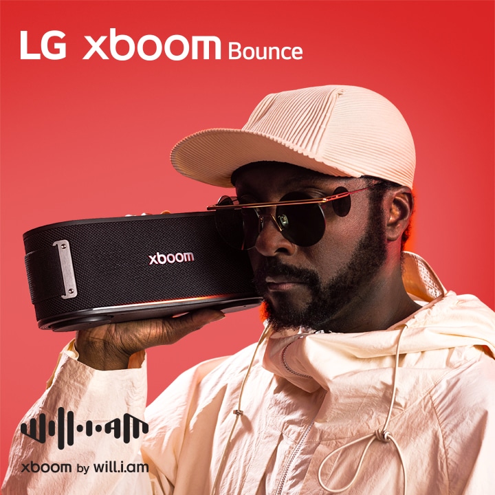 will.i.am, con un atuendo blanco y gafas de sol, está sosteniendo el xboom Bounce justo al lado de su rostro.