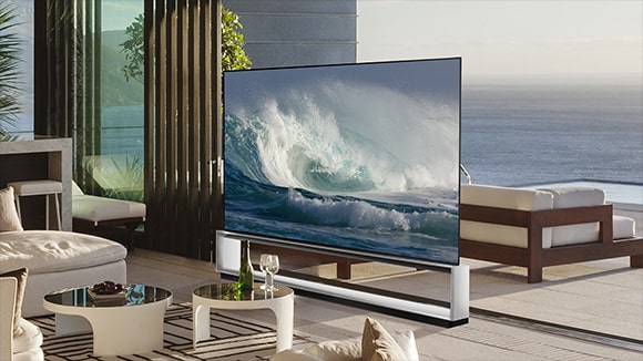Un TV LG OLED Z2 está en una habitación blanca minimalista delante de una ventana con vistas a un bosque.