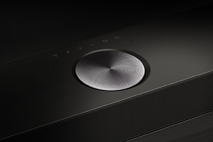 Detail jednoho z reproduktorů na zařízení LG Soundbar. Kousek nad reproduktorem jsou vidět ovládací prvky soundbaru. 