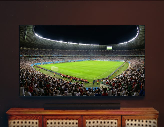 Televizor zobrazující panoramatický pohled na fotbalový stadion během zápasu