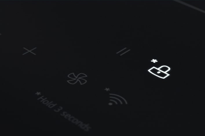 Toto je detailní snímek LED kontrolky s ikonou zámku, kterou lze nastavit tak, aby zabránila nechtěnému dotyku ovládacího panelu indukční varné desky.