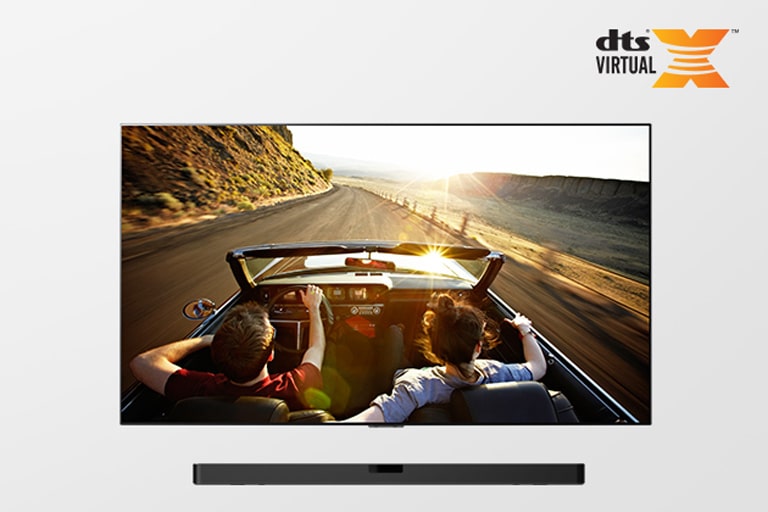 Celkový záběr na televizor a zařízení soundbar. Na obrazovce je pár v kabrioletu, jedoucí po silnici směrem k západu slunce.
