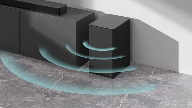 Na skříňce se nachází soundbar. Vedle stojí na podlaze bezdrátový subwoofer. Ze subwooferu vychází grafické zpracování modré zvukové vlny.