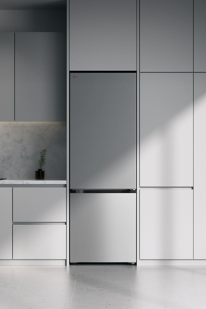 Stříbrná lednice s mrazákem LG zajíždí do moderní minimalistické kuchyňské skříňky v šedé kuchyni s kamenným obkladem.