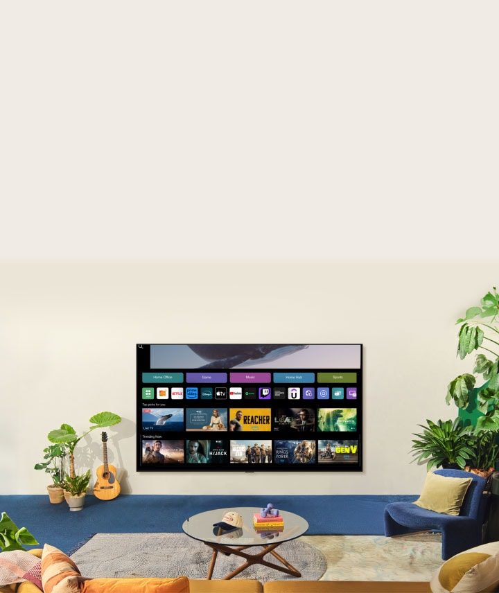 Ein über dem Ozean schwebender Wal und eine Frau im Ozean werden gezeigt. Ein Startbildschirm erscheint von unten. Beim Übergang der Szene wird das Bild auf einem großen LG TV an der Wand angezeigt. Zwei Frauen sitzen in einem gemütlichen und neutralen Wohnzimmer, das mit Pflanzen und einer Gitarre gefüllt ist. Eine Frau zeigt mit der Fernbedienung auf den Fernseher, der auf dem Startbildschirm eine Reihe von Apps und empfohlenen Fernsehsendungen anzeigt.