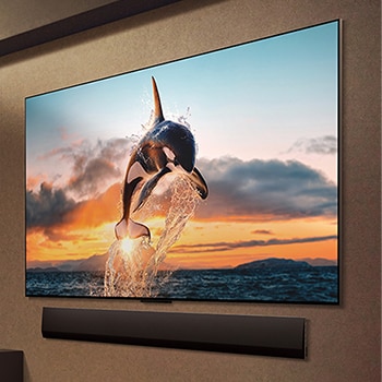 Geräumiges Wohnzimmer mit Blick auf eine Stadtlandschaft. Der LG OLED TV ist mit einer LG Soundbar an der Wand befestigt. Das flächenbündige Design des Fernsehers ermöglicht eine bündige Montage an der Wand und fügt sich gut in den Raum ein. Die Zero Connect Box ist zu sehen, aber unauffällig aufgestellt. 
