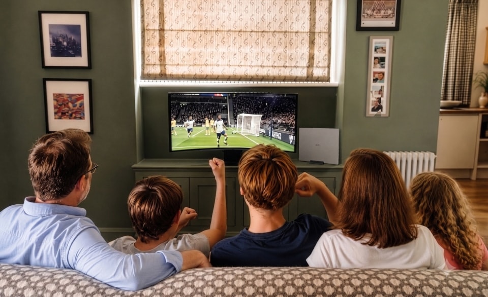 Die Familie Ferguson schaut sich gemeinsam ein Fußballspiel auf einem LG UltraGear Monitor in ihrem Wohnzimmer an.