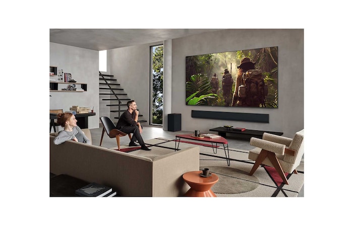 Wide view of a living room inside a premium home, a man is watching a movie on his wall-mounted LG OLED TV. The TV's design blends elegantly with the wall and the interior design.